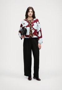 Cardigan de malha com padrões florais azuis e burgundy, combinado com calças largas pretas e uma mala preta estruturada. Sapatos vermelhos escuros.