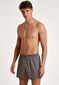Boxershorts in marineblauw met een geometrisch patroon in beige. Gemaakt van lichtgewicht stof met een elastische tailleband en knoopsluiting aan de voorkant.