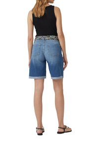 Bermudas de mezclilla en azul claro con dobladillos enrollados, bolsillos traseros y una cinturilla negra con patrón. Combinadas con una blusa sin mangas negra.