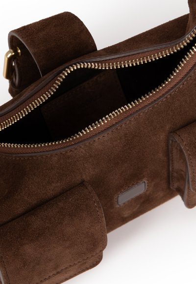 Brun ruskindshåndtaske med gylden lynlås, ottagonal form, to sidelommer og diskret logopatch på fronten. Indvendigt foret med mørkt stof.