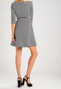 Robe rayée noir et blanc avec des manches trois-quarts, corsage cintré, jupe évasée et ourlet au genou. Associée à des sandales à talons noirs.