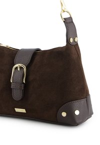 Sac à main en daim brun avec une base et une bandoulière en cuir foncé texturé. Il comprend une boucle dorée et des accents métalliques, avec une fermeture éclair.