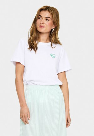 Witte katoenen T-shirt met korte mouwen, voorzien van een groen hartlogo. Gecombineerd met een lichtgroene gestreepte rok.