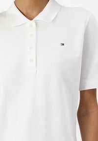Polo blanc à manches courtes avec un col, quatre boutons et un petit logo Tommy Hilfiger rouge, blanc et bleu sur la poitrine.