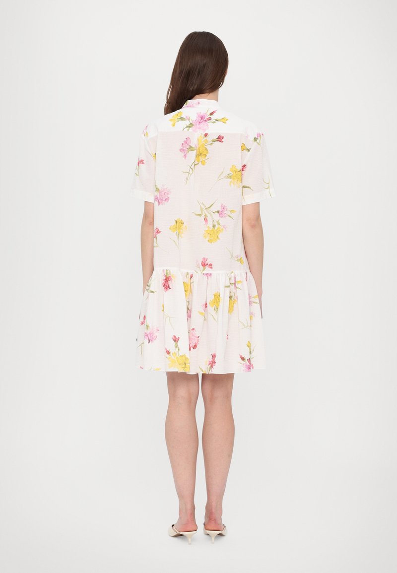 Robe blanche à manches courtes avec un motif floral en rose et jaune. Présente un volant en couches au niveau de l'ourlet et un col.