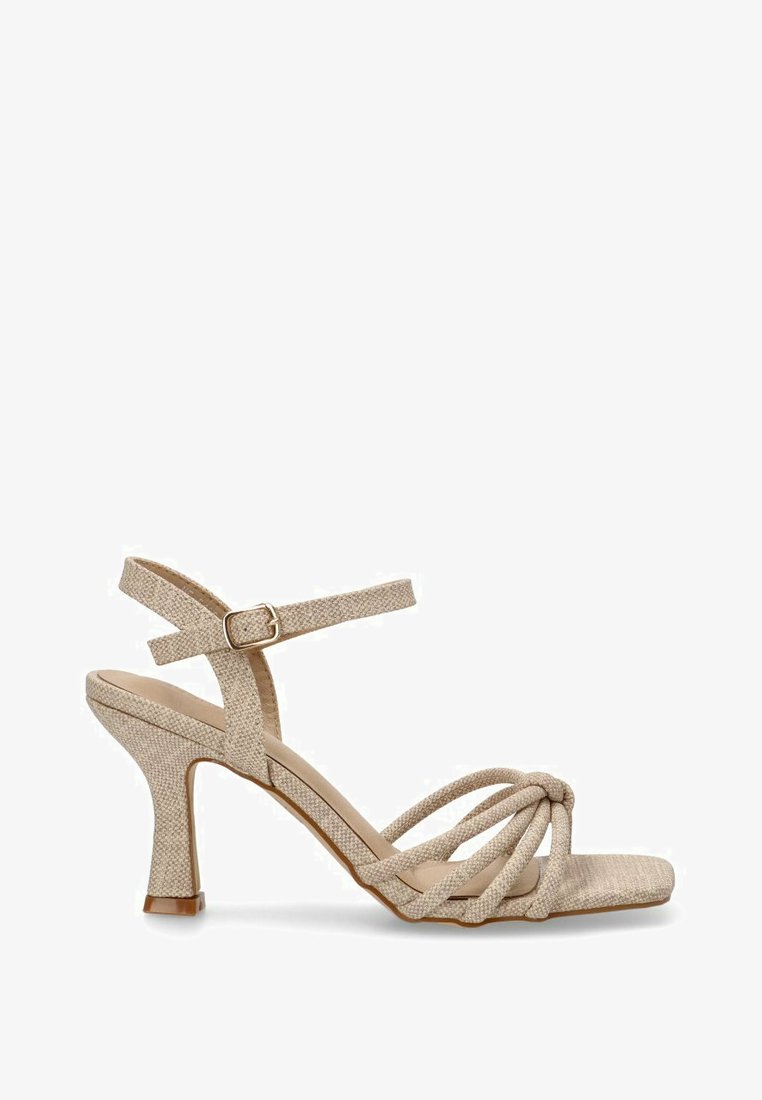 Sandalia de tacón alto beige con correas, fabricada en tejido texturizado, con correas enroscadas y un cierre en el tobillo. Presenta un tacón fino y una punta cuadrada.