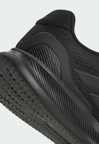 Černá sportovní bota s texturovaným síťovaným svrškem a gumovou podrážkou s vzorkem dezénu pro trakci a stabilitu.