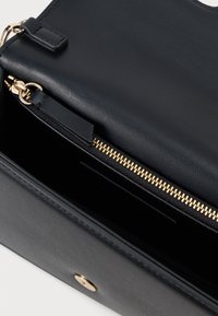 Fekete bőr kézi táska sima felülettel, arany cipzárral és patentos záródással. A belső tér kártyahelyekkel és bőséges hellyel rendelkezik.