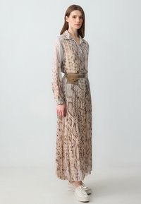 Maxi vestito con un leggero design plissettato in stampa serpente beige e marrone, completato da una cintura texturizzata e sneakers bianche.