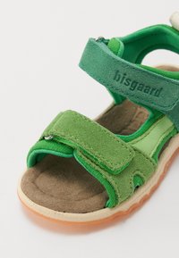 Green children's sandal made of suede and fabric, featuring adjustable Velcro straps and a cushioned insole with a rubber sole.