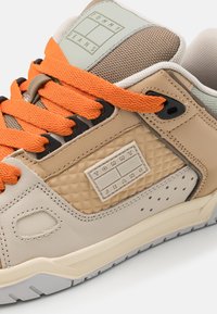 Beige lenkkarit, joissa on teksturoitu nahka ja verkko-osa, oranssit nauhat ja kumipohja. Sivussa on valkoinen logo-arkki.