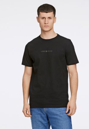 Sort bomulds T-shirt med korte ærmer og rund hals, med et diskret "LINDBERGH" logo i midten. Båret med blå jeans.