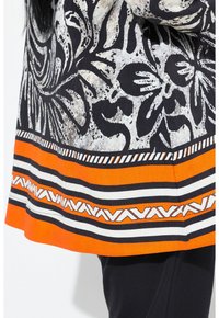 Zwart-wit gemusterde top met een oranje en witte gestreepte zoom en geometrische accenten. Textuurstof, levendige kleuren, casual ontwerp.