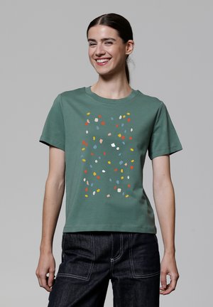 T-shirt en coton vert avec un motif de confettis multicolores sur le devant. Manches courtes, col rond, coupe décontractée et texture lisse.