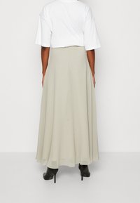 Flödande, lång A-linje kjol i ljusbeige tyg, ihop med t-shirt i lös passform i vitt. Tyget har en slät, mjuk känsla. Svarta högklackade stövlar syns.