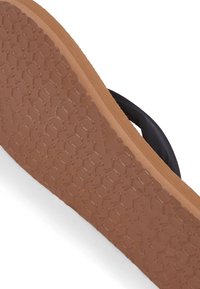 Schwarze Flip-Flops mit rutschfester Gummisohle, die ein braunes Grundmuster und einen glatten schwarzen Riemen aufweisen. Sichtbares, rutschfestes Profildesign.