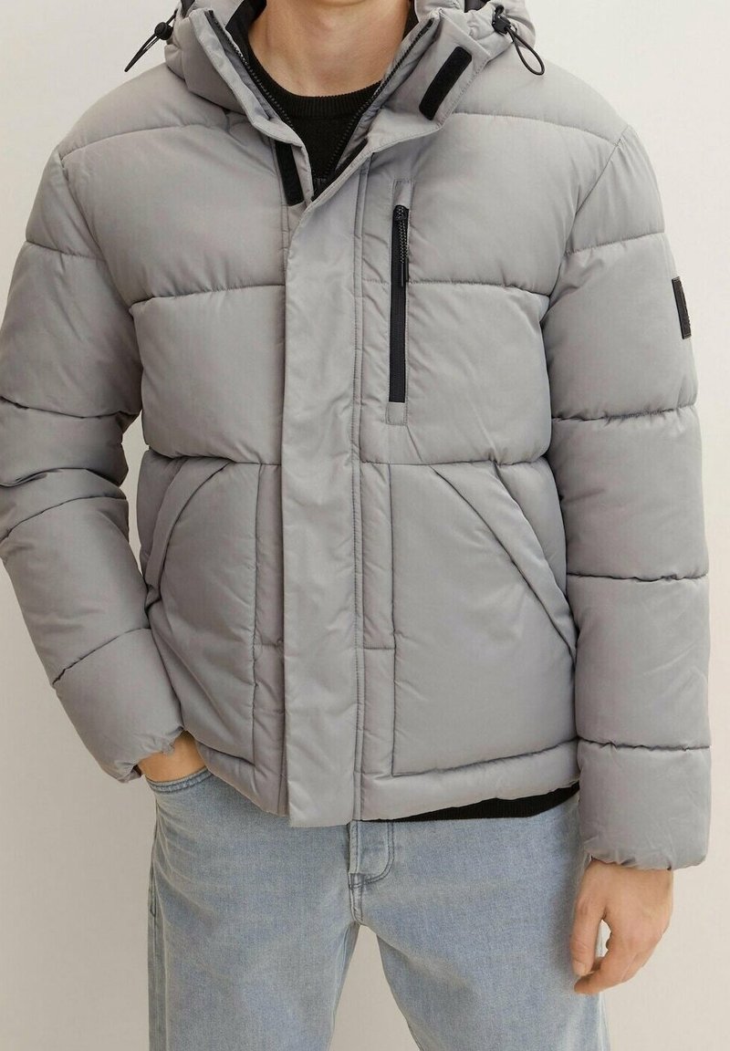 Szara kurtka puchowa z kapturem, z przeszywanymi panelami, kieszenią na piersi zapinaną na zamek, bocznymi kieszeniami oraz elastycznymi mankietami dla zapewnienia ciepła.