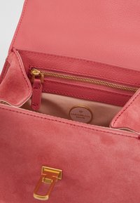 Sac à main en cuir rose avec une texture en daim, fermeture et zip en métal doré, avec un intérieur lisse et un détail du logo de la marque.
