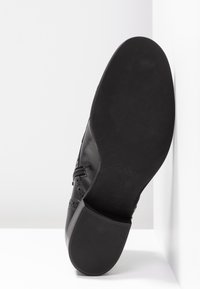 Černá kožená bota s texturovanou podrážkou, zdobená brogue detaily a zipovým zapínáním. Bota má elegantní, zaoblený tvar.