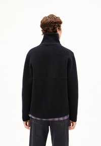 Pullover in pile blu scuro con colletto alto e finitura texturizzata. Presenta una vestibilità rilassata e un orlo leggermente curvo.