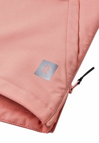 Vaaleanpunainen collegekangas, jossa on hopeinen logo neliön muotoisessa tarrassa, näkyvillä ompeleet ja musta vetoketju yksityiskohtana sivulla.