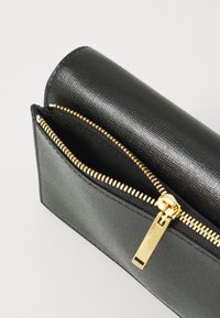 Carteira preta texturizada com fecho de zíper dourado. O interior é visível, apresentando um forro liso e compartimentos adicionais.