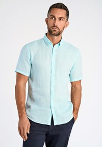 Lichtblauw overhemd met korte mouwen en knoopsluiting, gemaakt van een gestructureerde stof, met een kraag en een rechte zoom. Draagt bij donkere broek.