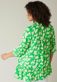 Blusa verde con un motivo floreale a margherite, maniche a tre quarti e orlo arricciato. Tessuto leggero con una vestibilità comoda.