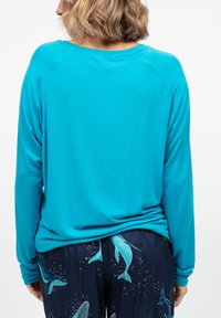 Camicia a maniche lunghe turchese con maniche raglan, caratterizzata da una vestibilità rilassata. Abbinata a pantaloni blu navy con un motivo di balene e accenti di stelle.
