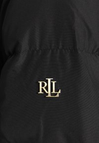 Tissu noir à texture lisse avec un logo métallique doré "RLL" cousu près de la couture, mettant en valeur la marque du vêtement.