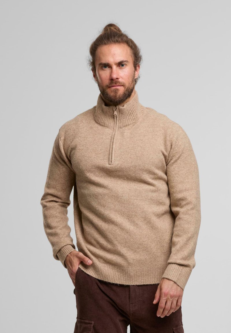 Beige wool zip-neck sweater with ribbed collar, fitted design, and contrasting stitch details. Paired with brown corduroy pants.