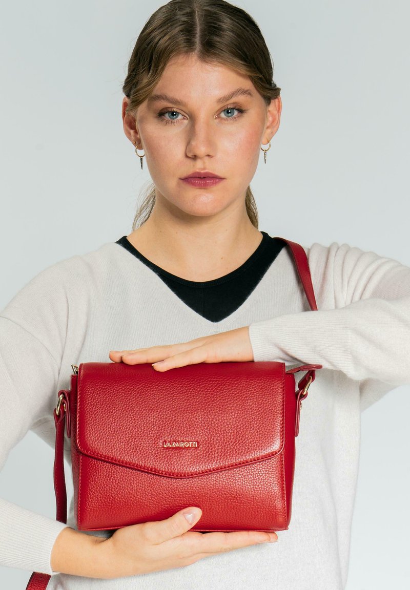 Bolso bandolera de cuero rojo con acabado texturizado, cierre magnético en la solapa y correa ajustable. Logotipo dorado en la parte frontal.