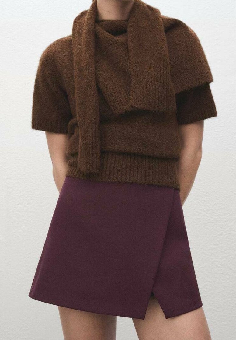 Pull marron en tricot à manches courtes avec un détail croisé, associé à une mini-jupe bordeaux ajustée comportant un ourlet diagonal.