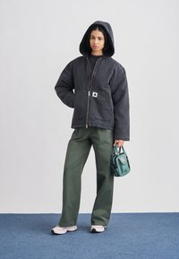 Juodas gobtuvuotas striukė su užtrauktuku ir tekstūruota medžiaga, laisvo kirpimo, derinama su žaliais plačiomis kelnėmis. Aksesuaras: mažytė žalsvai mėlyna rankinė.