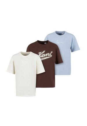 Drie T-shirts met korte mouwen en ronde hals in crème, bruin met "Kani 1989" logo, en lichtblauw, naast elkaar gerangschikt op een witte achtergrond.