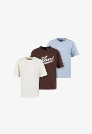 Drie T-shirts met korte mouwen en ronde hals in crème, bruin met "Kani 1989" logo, en lichtblauw, naast elkaar gerangschikt op een witte achtergrond.