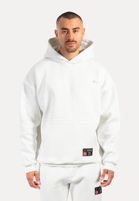 Felpa bianca con cappuccio realizzata in tessuto morbido, con tasca frontale, polsini a coste e un piccolo logo sul petto. Include etichette del marchio.