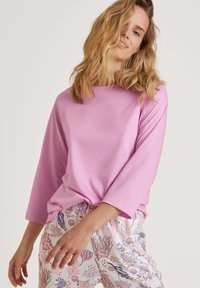 Lichtroze langemouwen top met een ronde halslijn, gecombineerd met een broek met een patroon van bloemmotieven in pasteltinten.