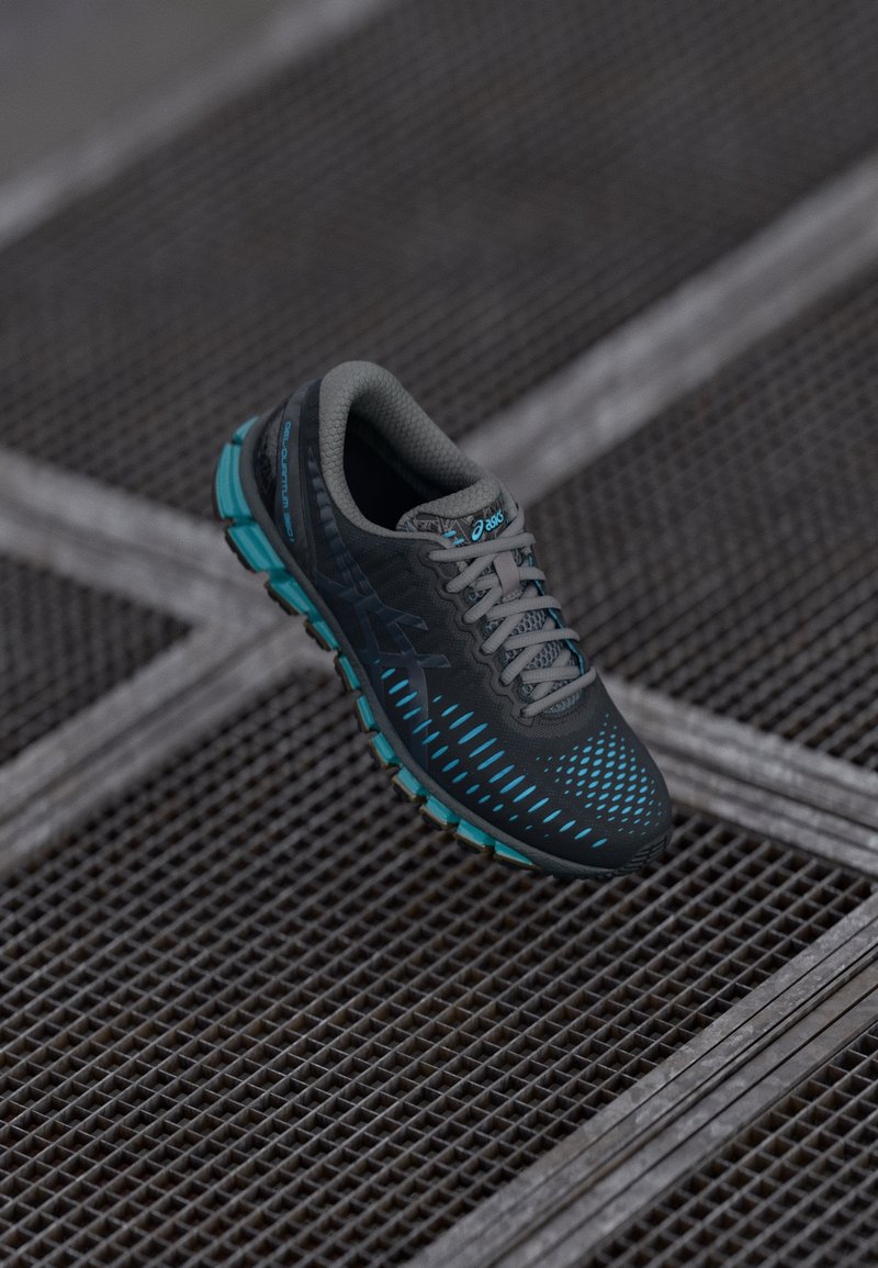 Chaussure de course Asics noire et bleue avec une semelle texturée reposant sur une surface en grille métallique avec des lignes qui se croisent.