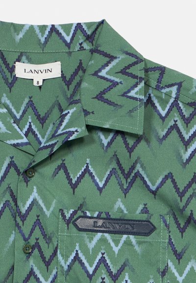 Πράσινο πουκάμισο με ζικ-ζακ μοτίβο, διπλωμένο γιακά, κουμπιά μπροστά, τσέπη στο στήθος και ετικέτες της μάρκας στον γιακά και την τσέπη.