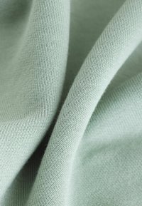 Hellgrüner Stoff mit einer weichen, glatten Textur, der ein feines Strickmuster und sanft fallende Falten zeigt.