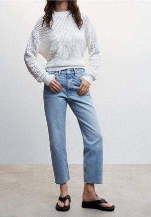 Valkoinen neulottu neule teksturoidulla kuviolla, yhdistetty vaaleansinisiin korkeavyötäröisiin farkkuihin ja mustiin tasapohjaisiin sandaaleihin. Rento ja väljä istuvuus.