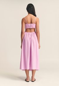Completo rosa a due pezzi con top arricciato e bottoni e gonna fluida di lunghezza media. Il materiale sembra leggero e leggermente strutturato.