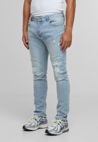 Light blue ripped skinny jeans with fading, five-pocket design, and a button closure. Worn with silver sports shoes.
