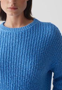 Maglione blu lavorato a maglia con un motivo testurizzato, dotato di un colletto a girocollo a coste e maniche lunghe. Il materiale appare leggero e traspirante.