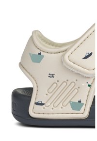 Ανοιχτό μπεζ σανδάλι με γραφικά βάρκας, λουράκι με βέλκρο, υφή στη σόλα και επένδυση με μαξιλάρι. Διαθέτει σκούρα μπλε βάση και διακριτικά σχέδια.