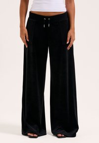 Schwarze weit geschnittene Hose aus weichem Material, ausgestattet mit Fronttaschen und einem verstellbaren Bund. Entworfen für Komfort und eine mühelose Passform.