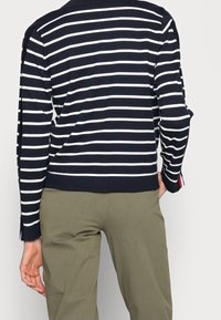 Randig tröja med långa ärmar i marinblått och vitt, med ribbad fåll och sidospår, matchad med olivgröna byxor.