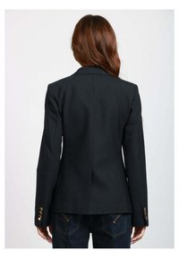 Blazer nero su misura con un design aderente, apertura centrale posteriore e dettagli con bottoni dorati sulle maniche. Realizzato in un tessuto liscio.