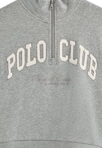 Sudadera gris con cuello de media cremallera. Presenta "POLO CLUB" en letras en relieve y "Beyond Classic" bordado debajo. Textura suave.